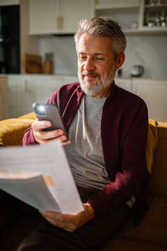 Mature man scanning bill with smartphone at home