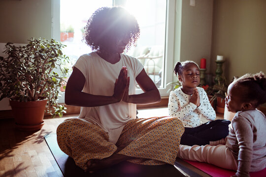 Mother and daughters meditating on yoga mats at home
