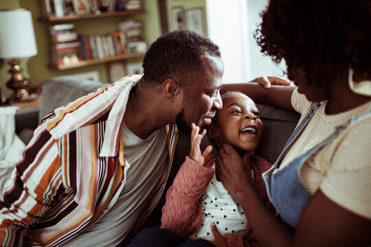 Parents tickling daughter on living room sofa