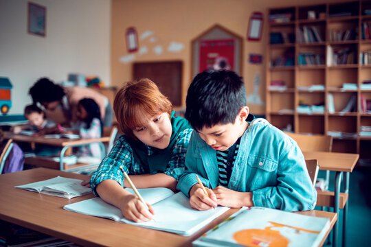 Two boys studying and writing together in classroom
