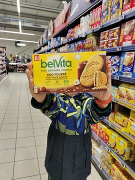 Saujon, France - January 24, 2026: Intermarche. Child holding belVita Duo Fourre chocolate biscuits box in a grocery store aisle with various snacks displayed in the background
