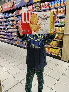 Saujon, France - January 24, 2026: Intermarche. Child holding LU Petit Beurre cookie box in a grocery store aisle with various products visible on shelves behind