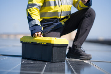 Fototapeta premium Worker crouching beside solar panels while opening a yellow toolbox