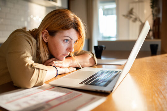 Stressed woman looking at laptop over household bills at home