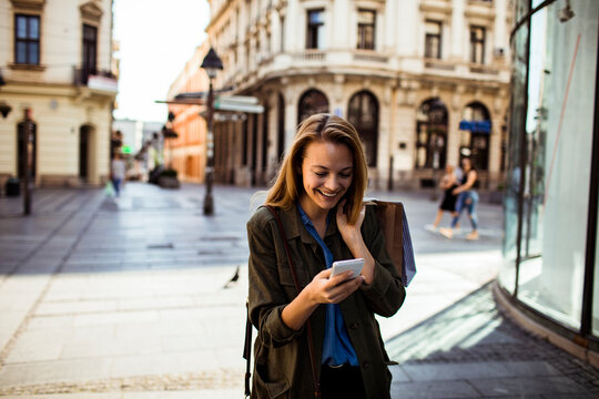 Smiling young woman using smartphone on city shopping street