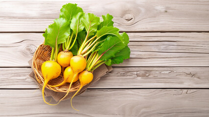 Freshly harvested golden beets with vibrant green leaves resting in a wicker basket on a rustic wooden table