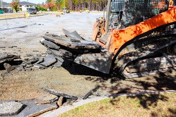 Skid steer machinery works to break up remove old asphalt at construction site in residential neighborhood. © ungvar
