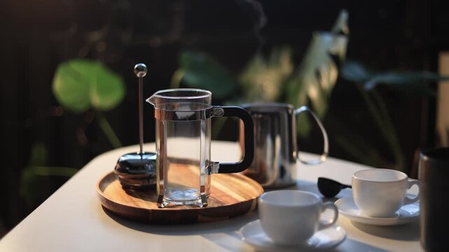 Hand pressing plunger on French press coffee maker with steam rising outdoors