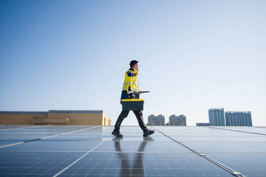 Engineer carrying toolbox walking across rooftop solar panels for inspection