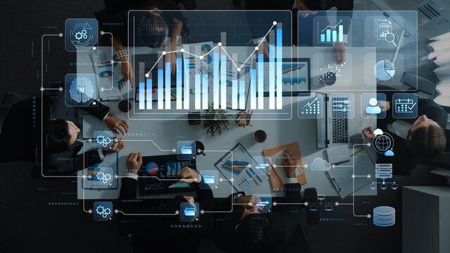 Aerial view of a diverse business team engaged in a meeting, analyzing data and charts presented on digital displays in a contemporary office environment. Raster