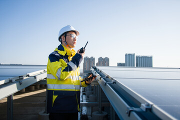 Engineer inspecting solar photovoltaic power station on rooftop while holding a walkie-talkie