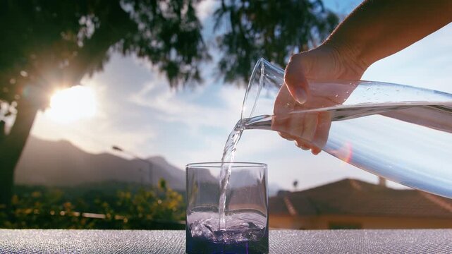Female Outdoors Holding Jug and Filling Glass with Fresh Water in Homely Setting