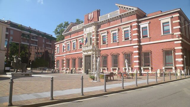 Courthouse in Varese Italy, exterior facade of red brick tribunal building in Piazza Cacciatori delle Alpi, Italian and European Union flags waving, sunny summer day, empty square, government and just
