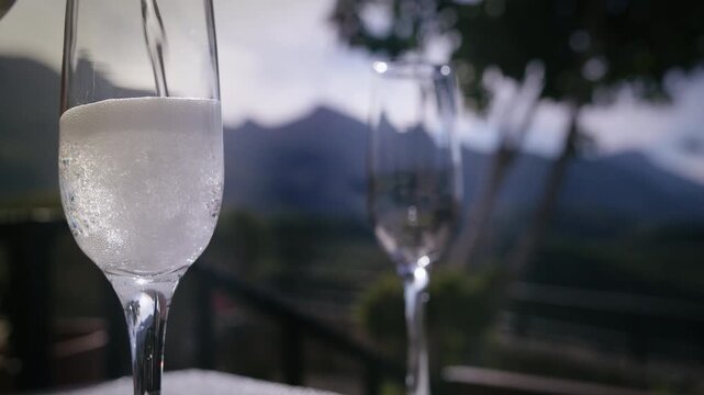 Sparkling Champagne Being Poured into Glass Outdoors with Scenic Mountain View in Background