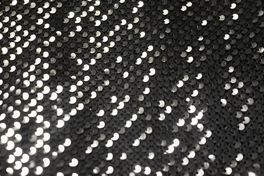 Black glittering sequin fabric texture with sparkling light reflections background