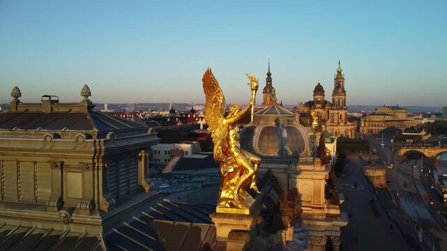 A circular aerial shoot of the statue of golden angel Phantasosone on the western corner risalit of the Dresden Art Academy  in the Lipsiusbau building under sunshine at dawn with the Frauenkirche, Dr
