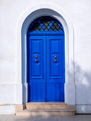 Fototapeta premium Blue double door with metal knockers under arch in white facade with stone steps.