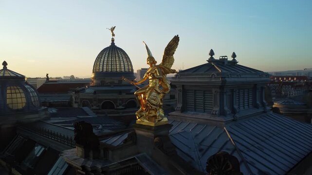 A circular aerial shoot of the statue of god Phantasos on the western corner risalit of the Dresden Art Academy  in the Lipsiusbau building under sunshine at dawn with the Frauenkirche, Dresden's Old 