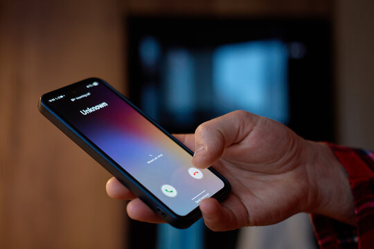 Closeup of hand holding smartphone with unknown incoming call on screen indoors. Concept of mobile communication, spam call and privacy risk