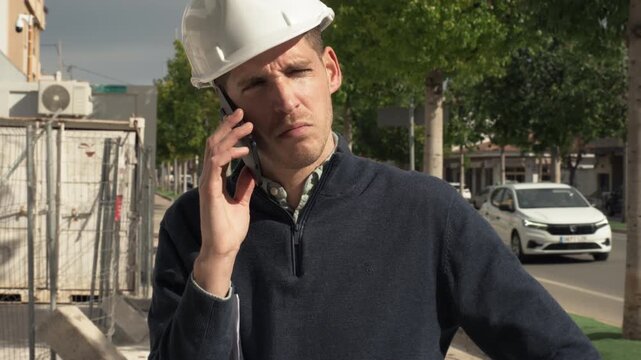Construction site manager talking on smartphone outdoors. Professional coordination of building project and contractor communication.