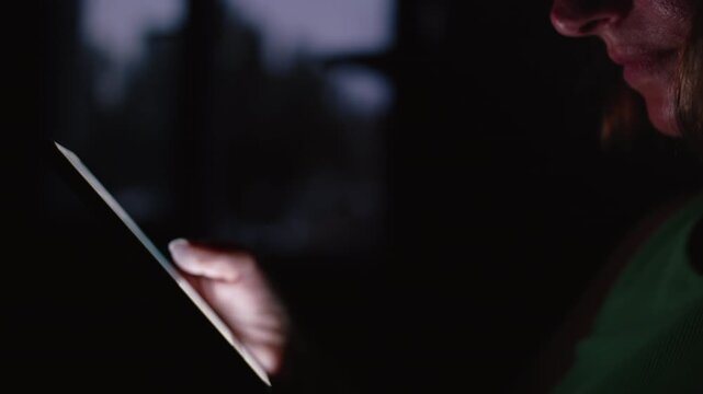 Woman Holding Mobile Device at Night Near Glass Window with City Lights Reflected