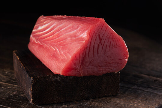 A large piece of fresh tuna. A fresh piece of tuna on a wooden board. A useful omega. Dark background.