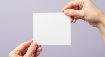 Obraz premium Hands holding a blank white card against a soft lavender background from a frontal viewpoint