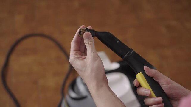 Person preparing for household deep cleaning, attaching brush attachment to steam cleaner nozzle before sanitizing surfaces and removing deep dirt, close-up. Concept of domestic hygiene, slow motion.