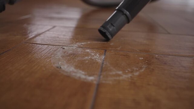 Vacuum cleaner nozzle sucking up white dust and small particles from household parquet floor, performing essential task of regular house cleaning and keeping tidy home, close-up, slow motion.