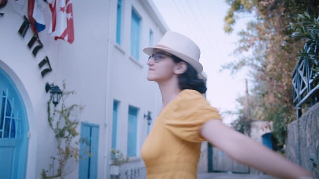 Cheerful Young Woman in Yellow Dress and Hat Joyfully Twirling on Charming European Alley