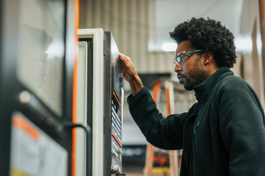 Low angle view of male metal worker examining machine while working at plant