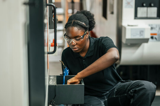 Concentrated young female worker examining mechanics while working in factory