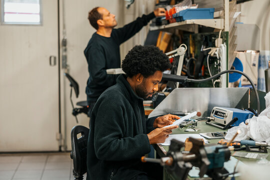 Focused male worker reading instructions of machine parts while working in factory plant