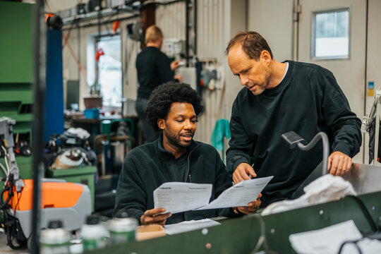 Multiracial male workers discussing instructions on paper before manufacturing products in factory