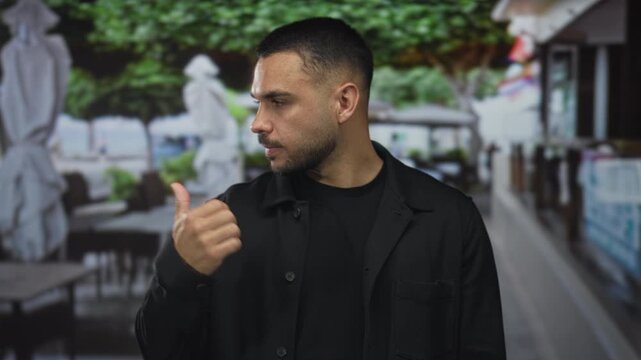 Man shows bare thumb up gesture on building terrace overlooking blurred tables and umbrellas; optimism.