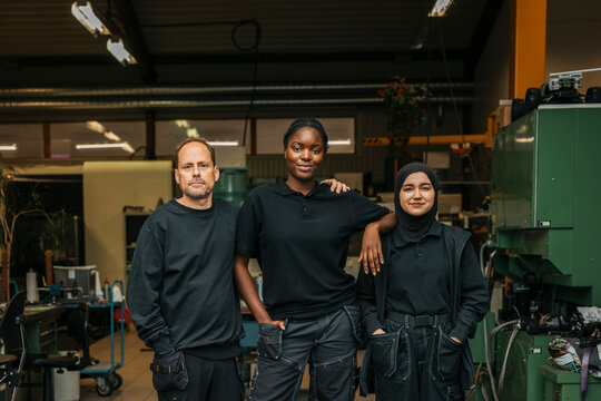 Portrait of confident multiracial male and female metal workers wearing uniform standing with each other