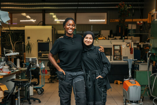 Portrait of smiling young female factory worker standing with arm around coworker