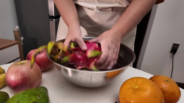 Close-up of a woman's hands , standing in front of a table with fruit and washing pitahaya