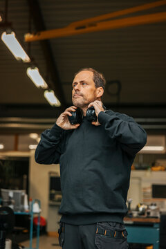 Mature male factory worker looking away while wearing ear protectors around neck