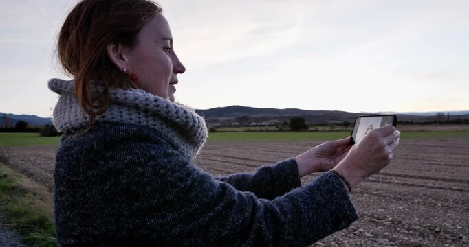 Capturing the Moment: A woman, engrossed in the simplicity of the moment, uses a mobile device to document a serene landscape, immortalizing the blend of nature and technology.