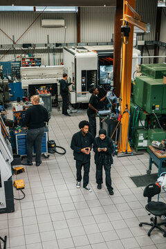 High angle view of male and female employees discussing with each other while walking in factory plant