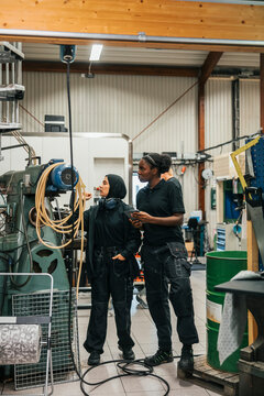Full length of female workers operating industry machine while working in factory