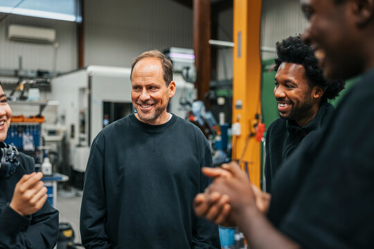 Smiling mature male worker standing with coworkers in factory
