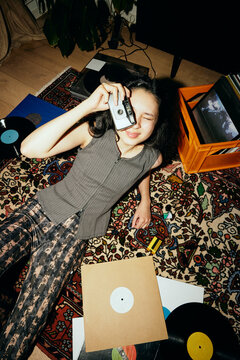 High angle view of woman looking through vintage camera while reclining on carpet at home