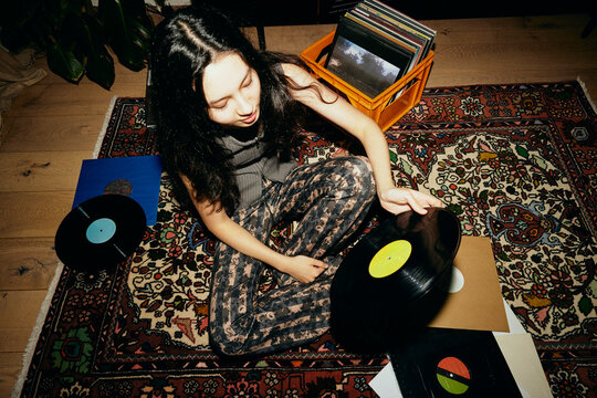 High angle view of young woman holding old vinyl record while sitting on carpet