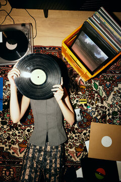 Directly above shot of woman covering face with vinyl record while lying on carpet