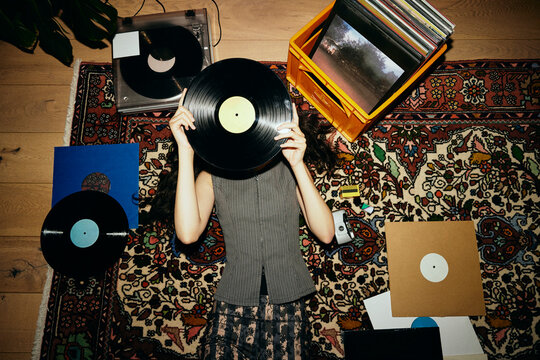 Young woman covering face with vinyl record while lying down on carpet
