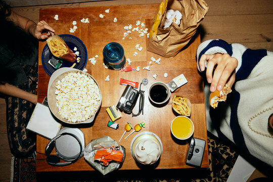 Directly above shot of young friends having fast food while sitting around messy table at home