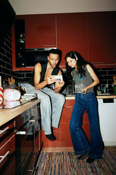 Full length of curious friends checking out music CDs in kitchen at home