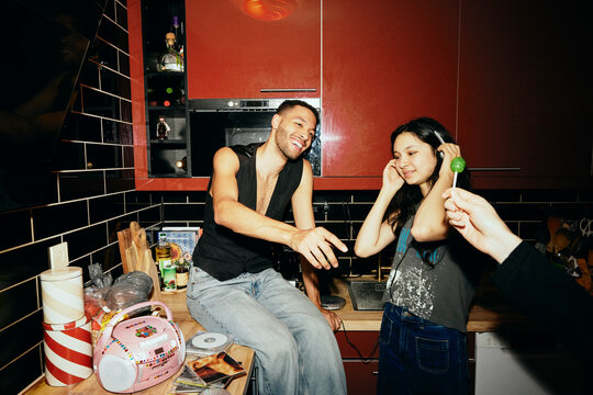 Smiling young man taking lollipop from friend in kitchen at home